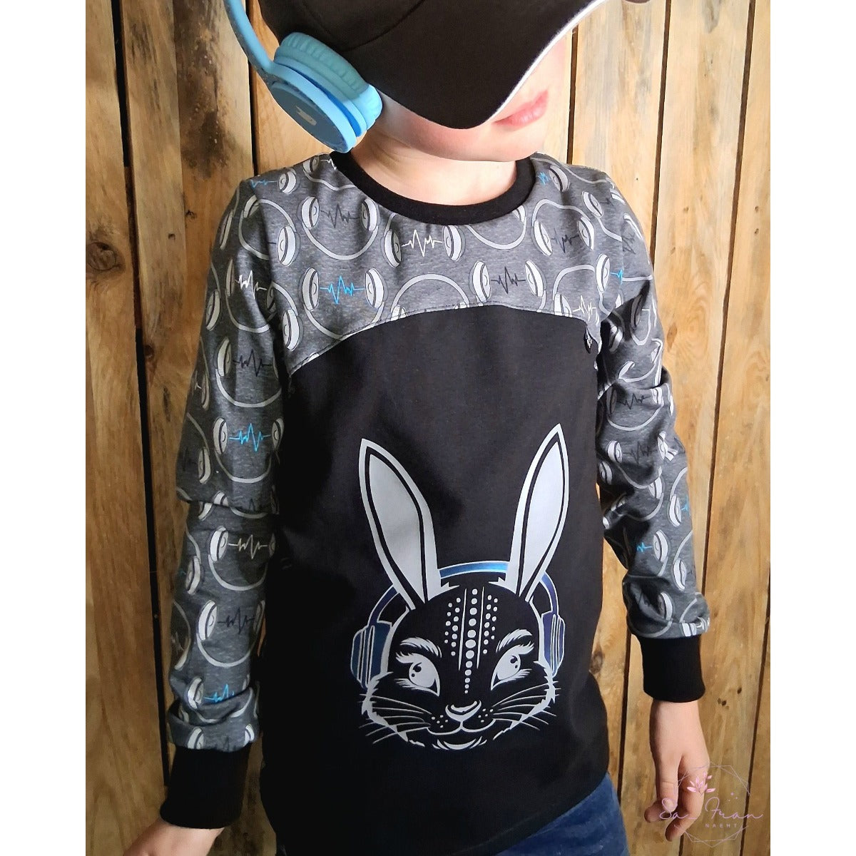 Junge im Raglanshirt in Schwarz und Grau mit Hasenkopf in Weiß und blauen Kopfhörern
