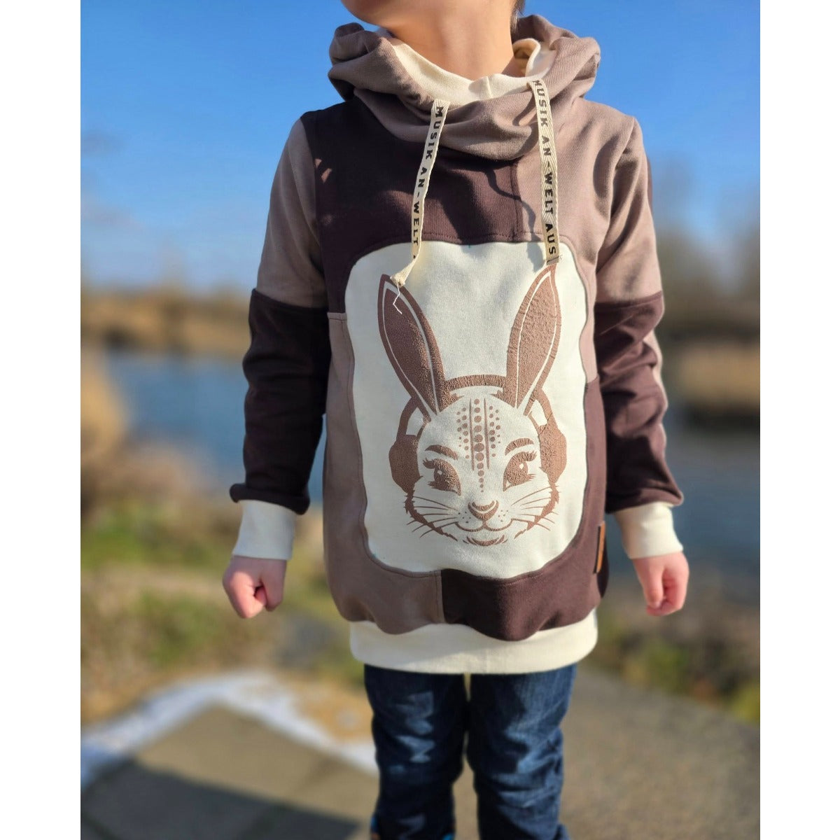 Kind im braunen Hoodie mit großer Hasen-Applikation auf der Vorderseite