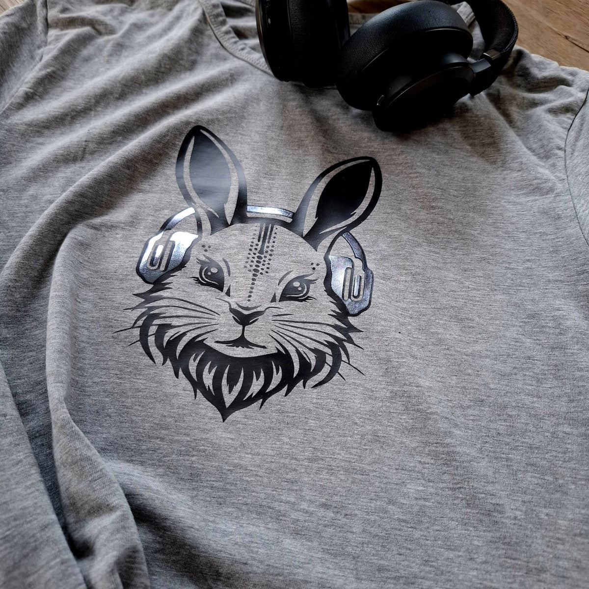 Graues Shirt mit Hasenkopf in Metallicfolie, daneben schwarze Kopfhörer