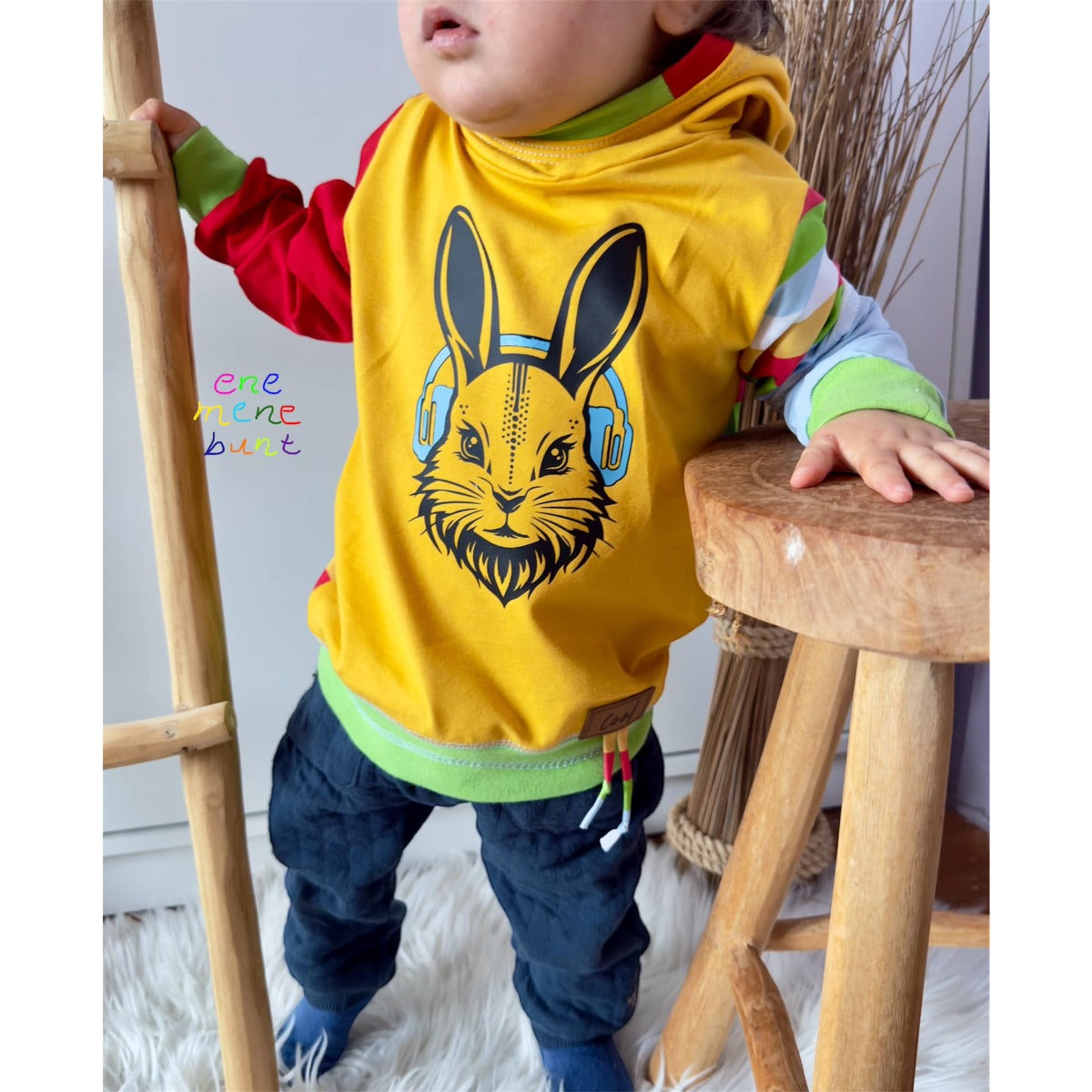 Kleinkind im gelben Shirt mit Hasenkopf und blauen Kopfhörern