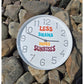 Weiße Wanduhr mit Plotterdatei „Less Drama More Sunrises" in bunten Retro-Buchstaben