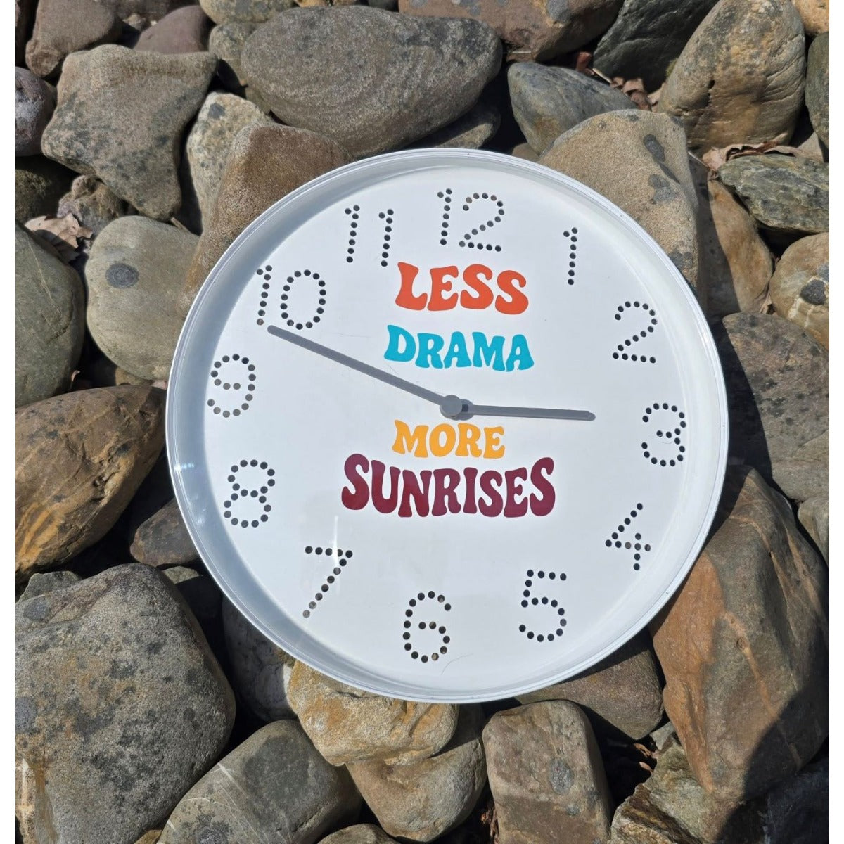Weiße Wanduhr mit Plotterdatei „Less Drama More Sunrises" in bunten Retro-Buchstaben