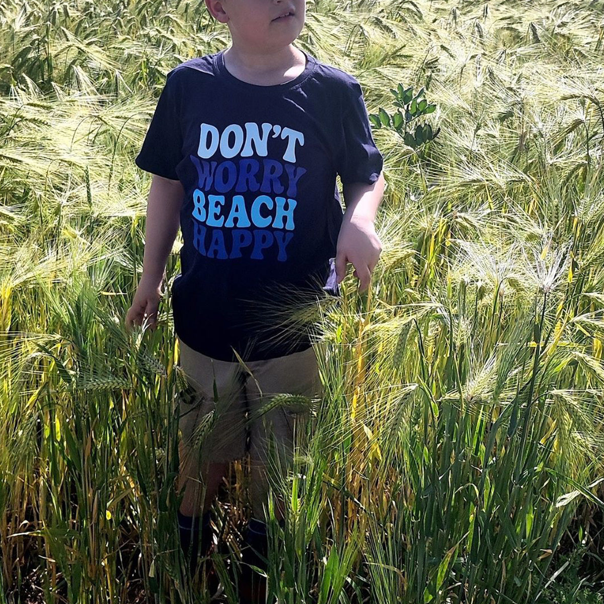 Junge im dunkelblauen Shirt mit Plotterdatei „Don't Worry Beach Happy" im Kornfeld