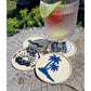 Vier helle Untersetzer mit Plotterdatei Sunset by the Sea, Palmen- und Wellenmotiv, neben Cocktailglas