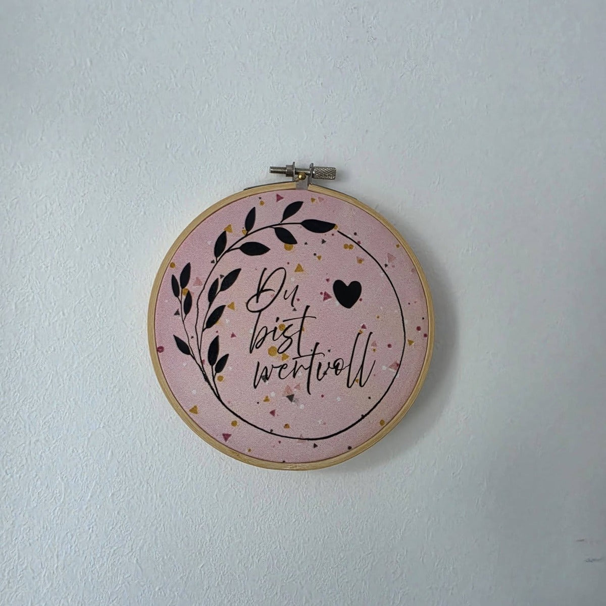 Plotterdatei Wertvolle Label – Motiv „Du bist wertvoll“ mit Blätterzweig, Kreis und Herz in Schwarz auf rosa Konfetti-Stoff im Stickrahmen
