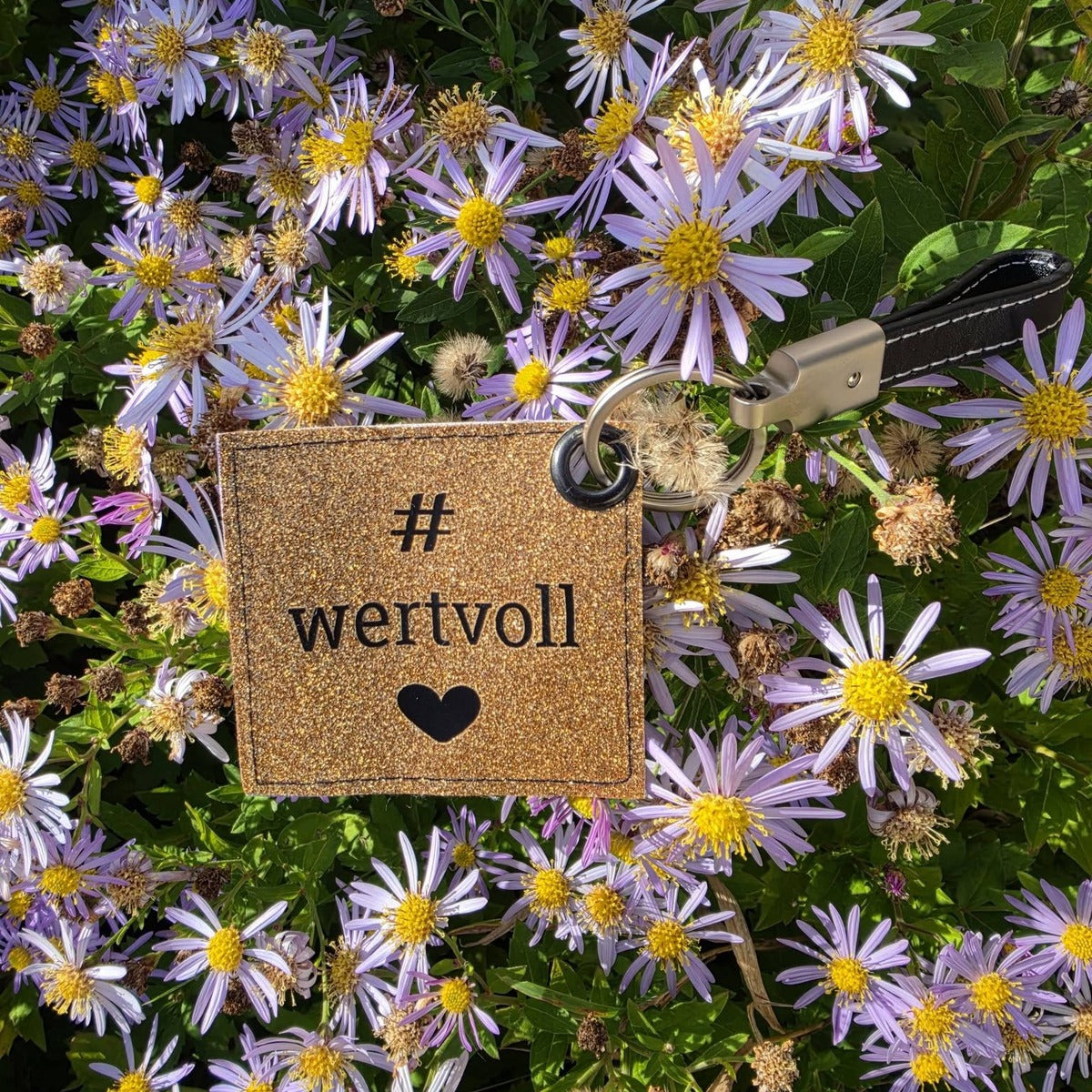 Plotterdatei Wertvolle Label – Schlüsselanhänger aus goldenem Glitzer-Kunstleder mit „# wertvoll“ und Herz zwischen lila Astern