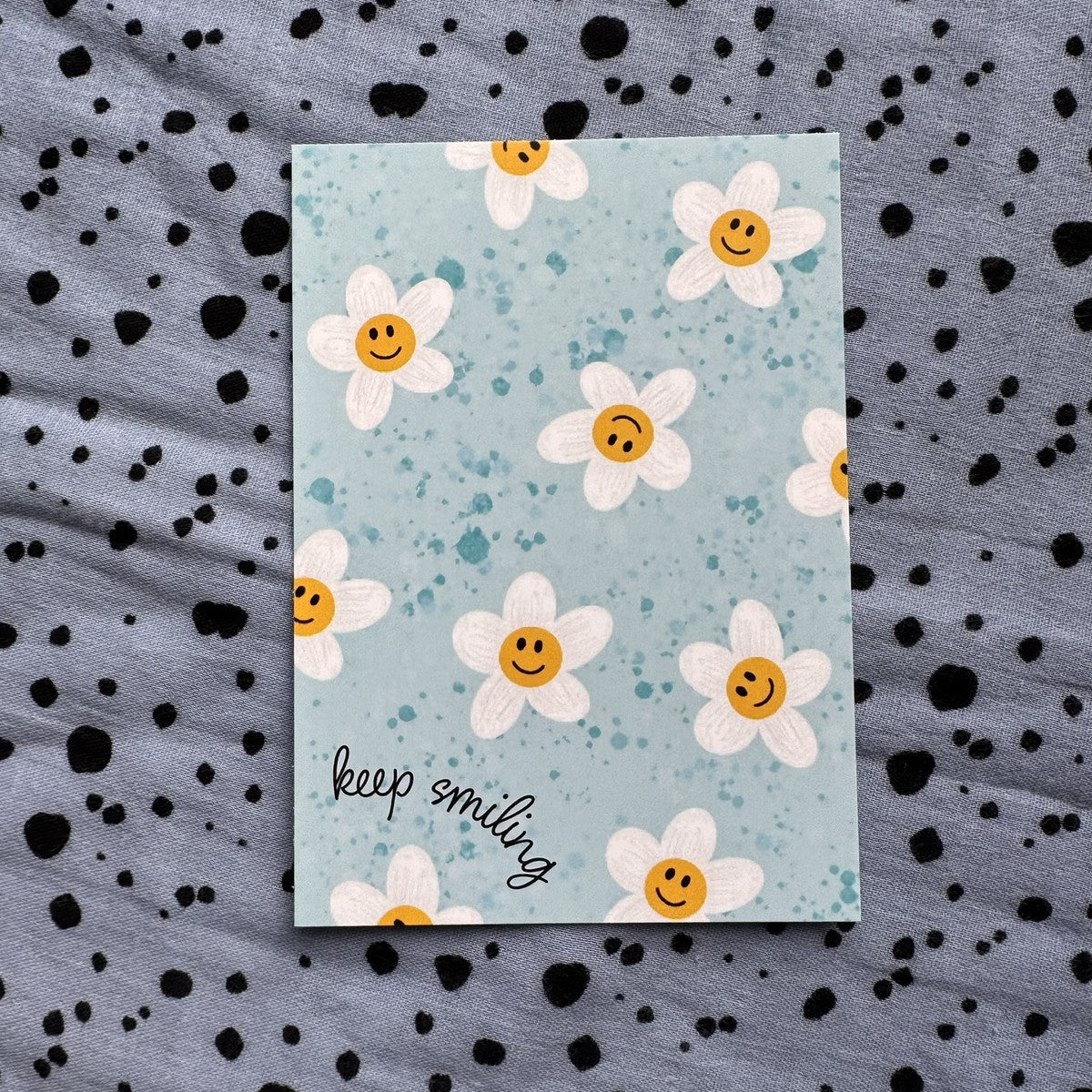 Postkarte keep smiling mit lachenden Gänseblümchen auf hellblauem Grund