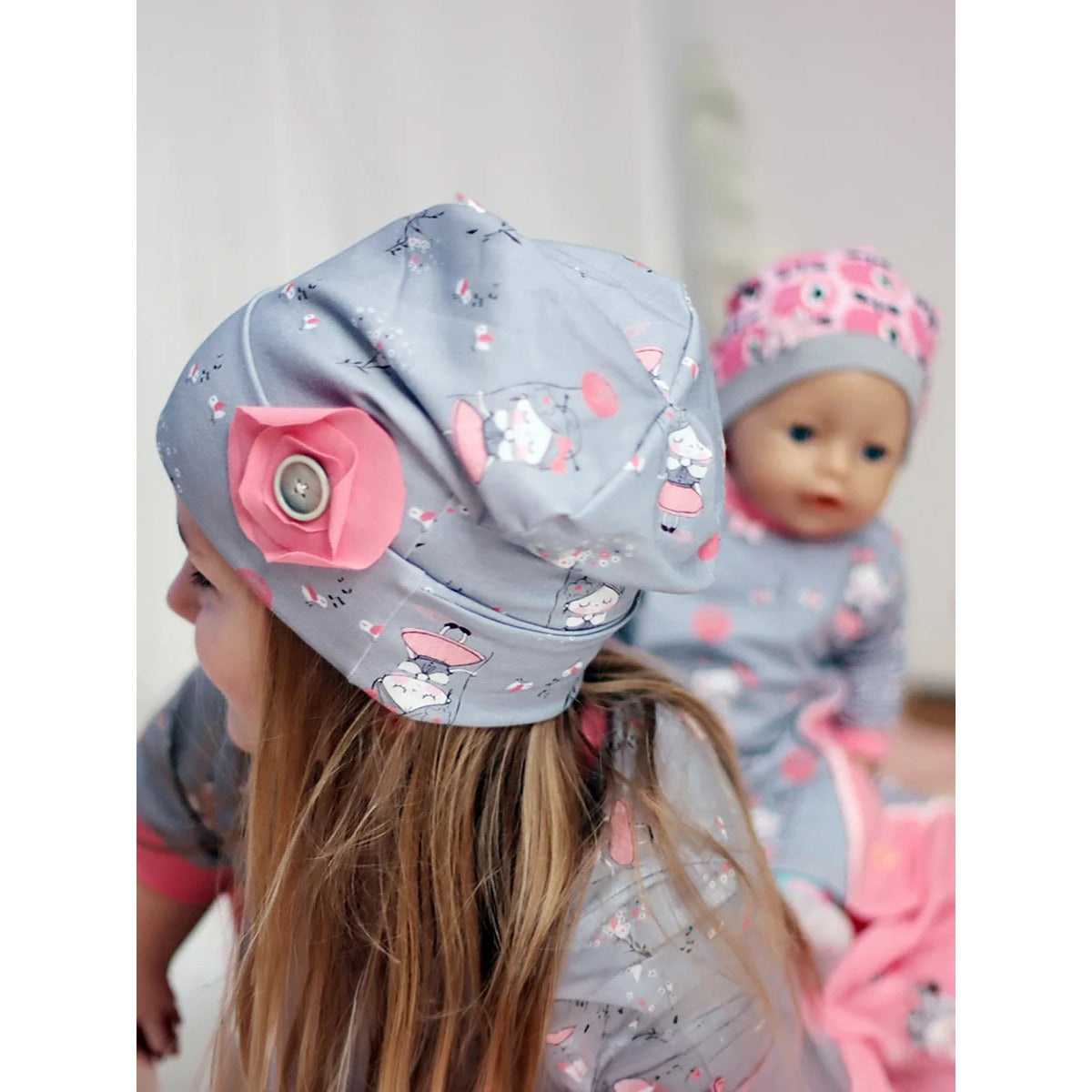 Beanie Bernie – graue Umschlagbeanie mit Mädchen-Ballon-Print und aufgenähter Stoffblume mit Knopf, dazu passende Beanie an der Puppe