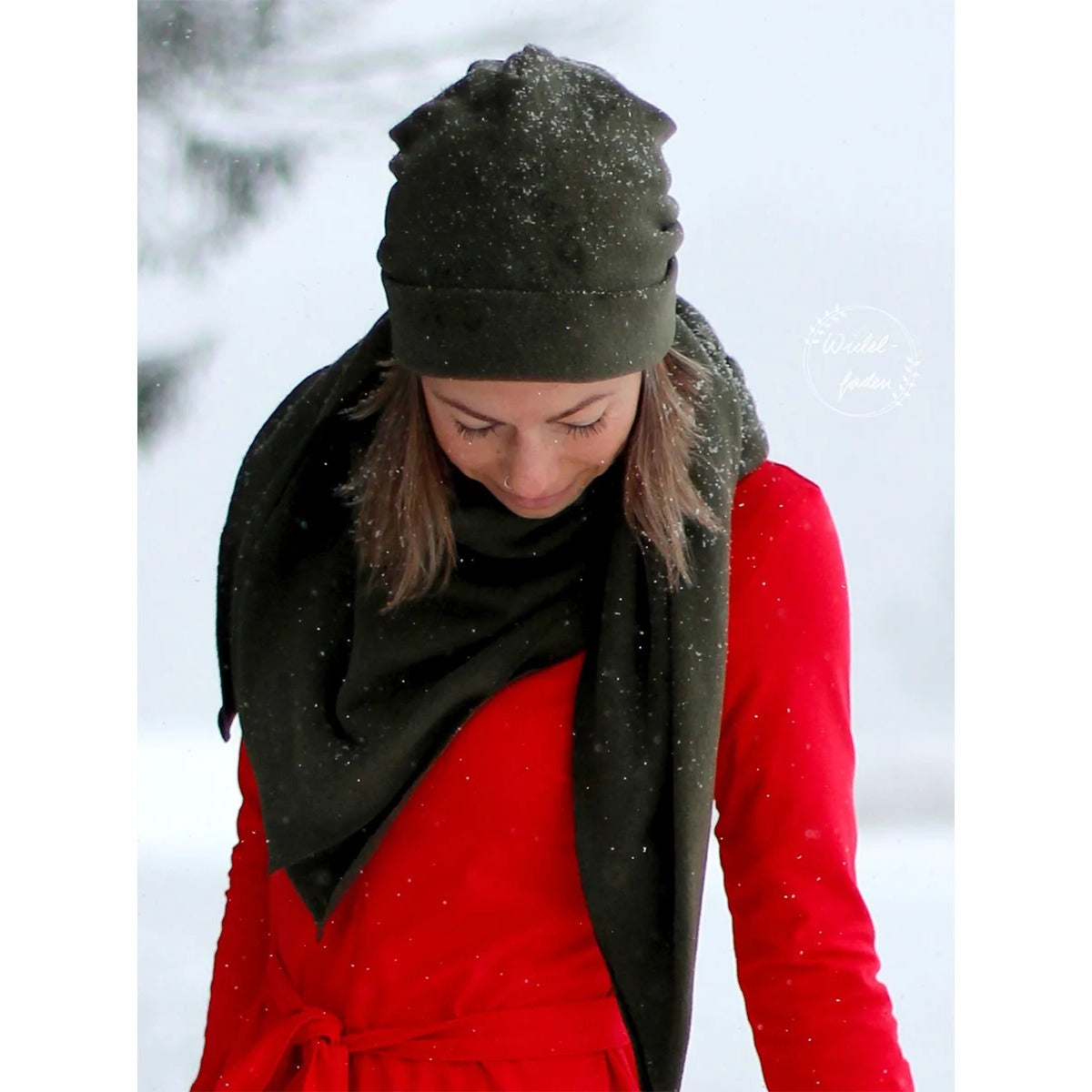 Beanie Bernie – khakifarbene Umschlagbeanie mit passendem Dreieckstuch, getragen von einer Frau im Schnee zum roten Kleid