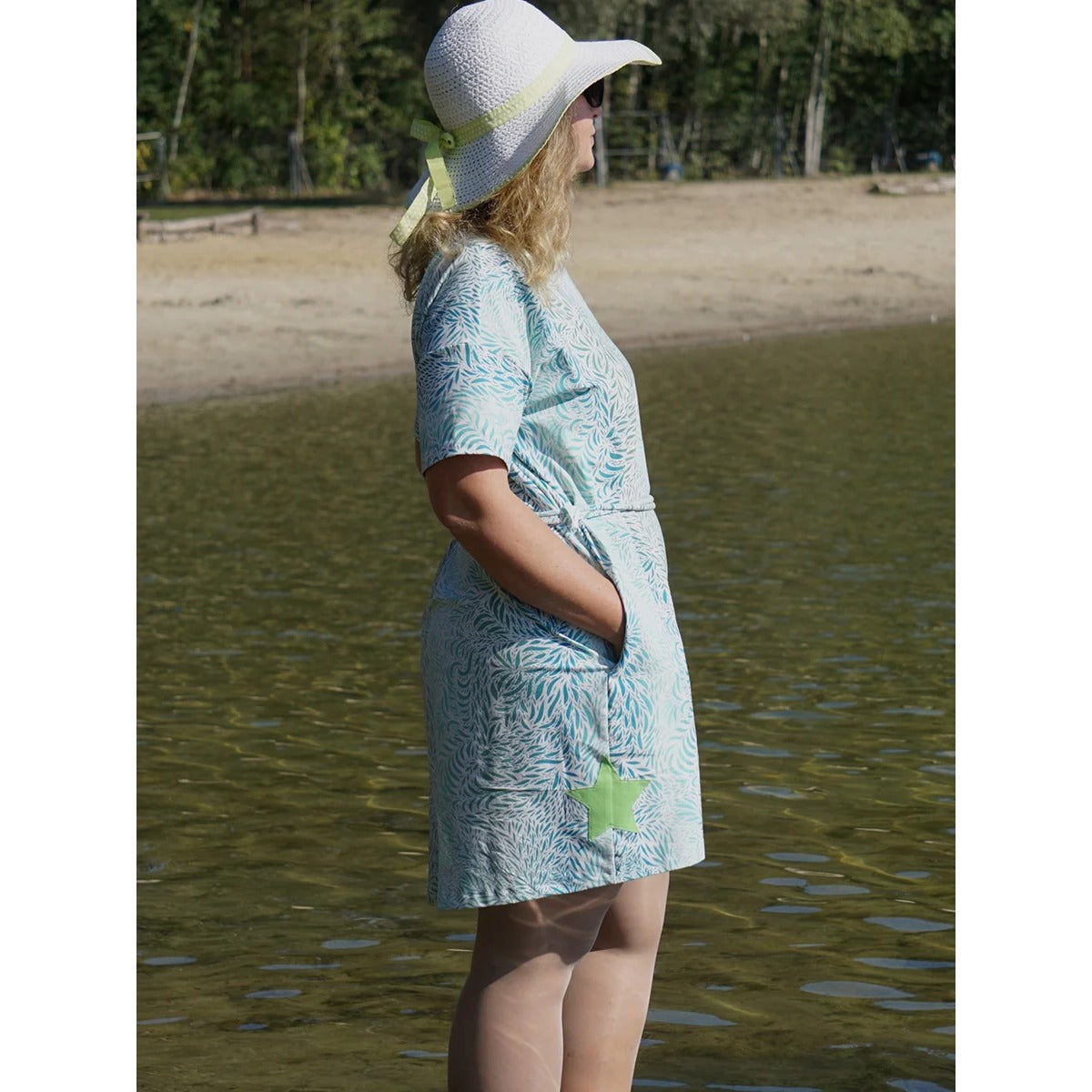 Cut Out Kleid – türkis gemustertes Kleid mit kurzen Ärmeln, Eingrifftaschen und appliziertem grünem Stern, Frau mit Sonnenhut im Wasser