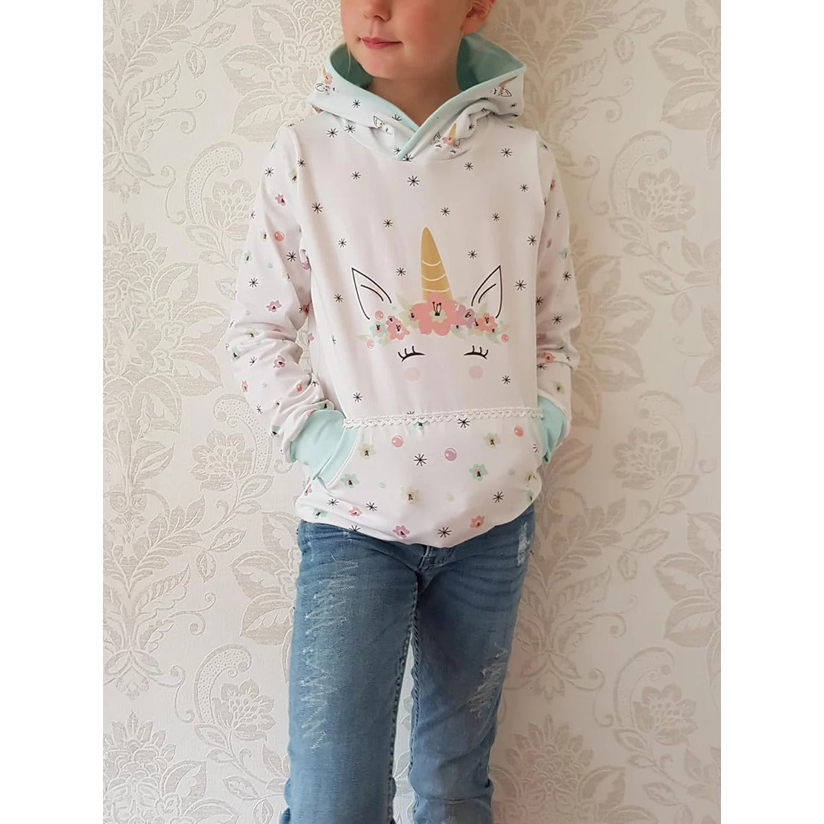 Lottchen Kinder als Hoodie aus weißem Jersey mit Einhorn-Print, Blüten- und Sternenärmeln, mintgrün gefütterter Kapuze und Kängurutasche mit Häkelborte
