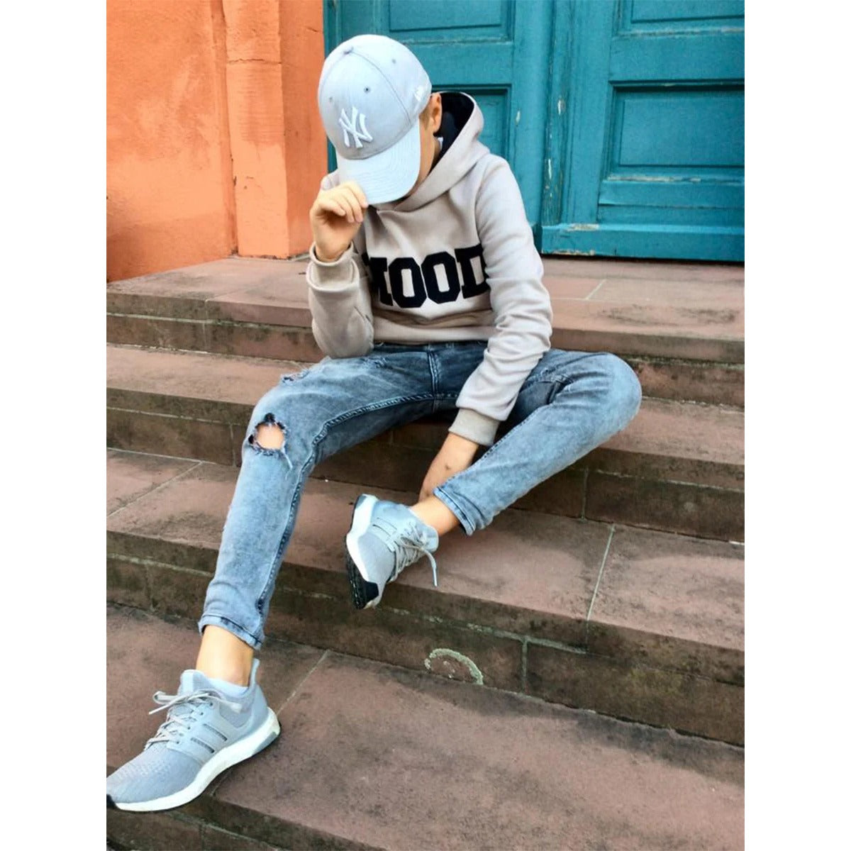 Lottchen Kinder als Hoodie für Jungs aus beigem Sweat mit großem MOOD-Print, Junge mit Cappy auf einer Treppe – der Schnitt ist unisex und jungstauglich