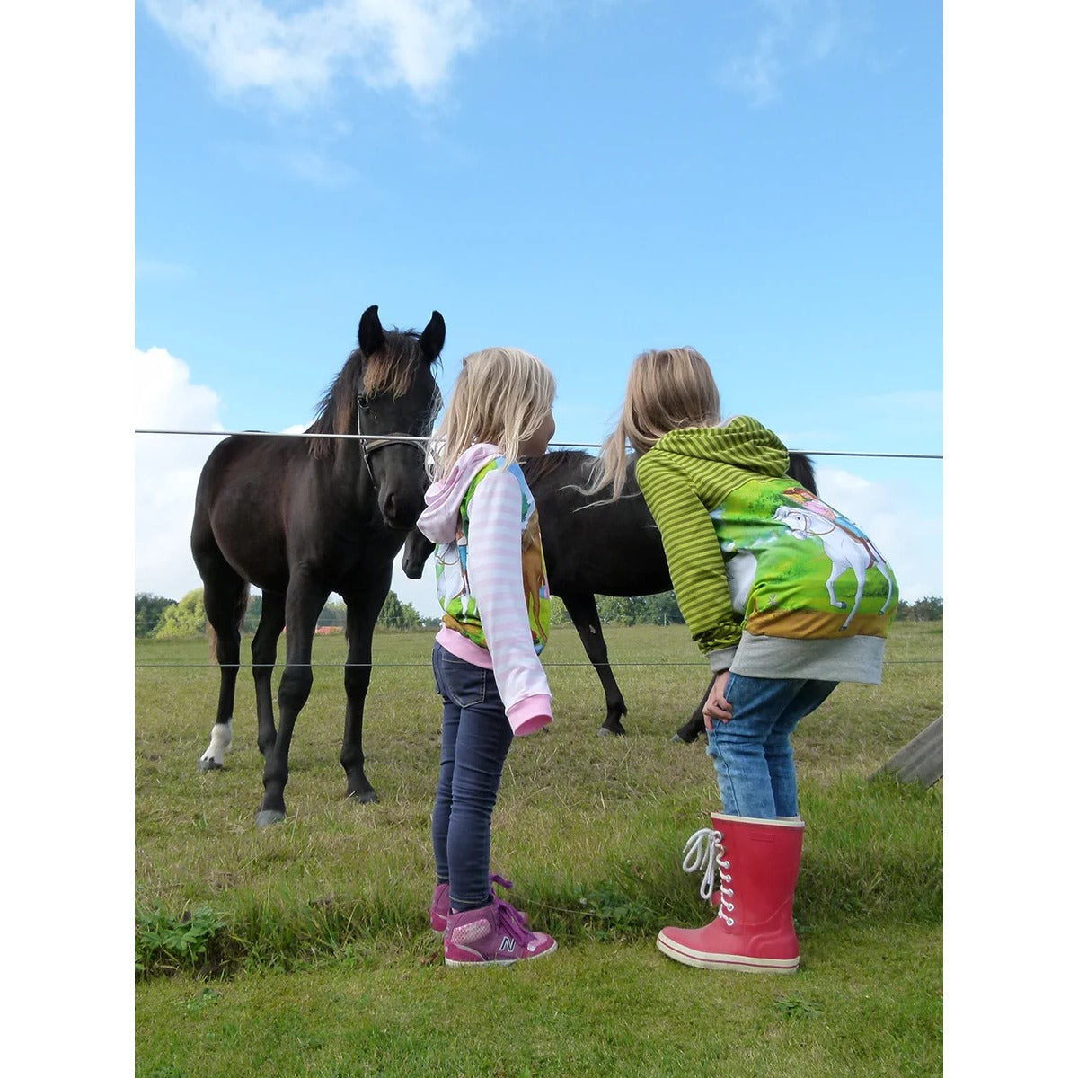 Lottchen Kinder als Hoodie und Hoodiekleid mit Pferde-Motiv im Rückenteil, rosa-weiß und grün geringelte Ärmel, zwei Mädchen an der Pferdekoppel
