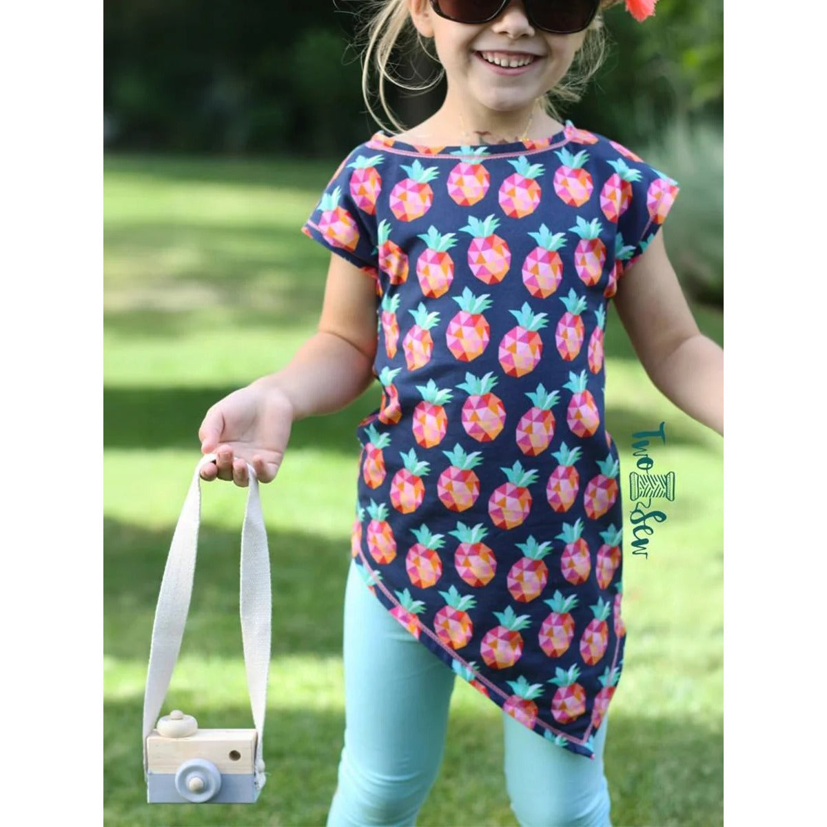 One Tip Shirt Kinder aus dunkelblauem Jersey mit buntem Ananas-Print, kurze überschnittene Ärmel und asymmetrischer Zipfelsaum, Mädchen mit Holzkamera