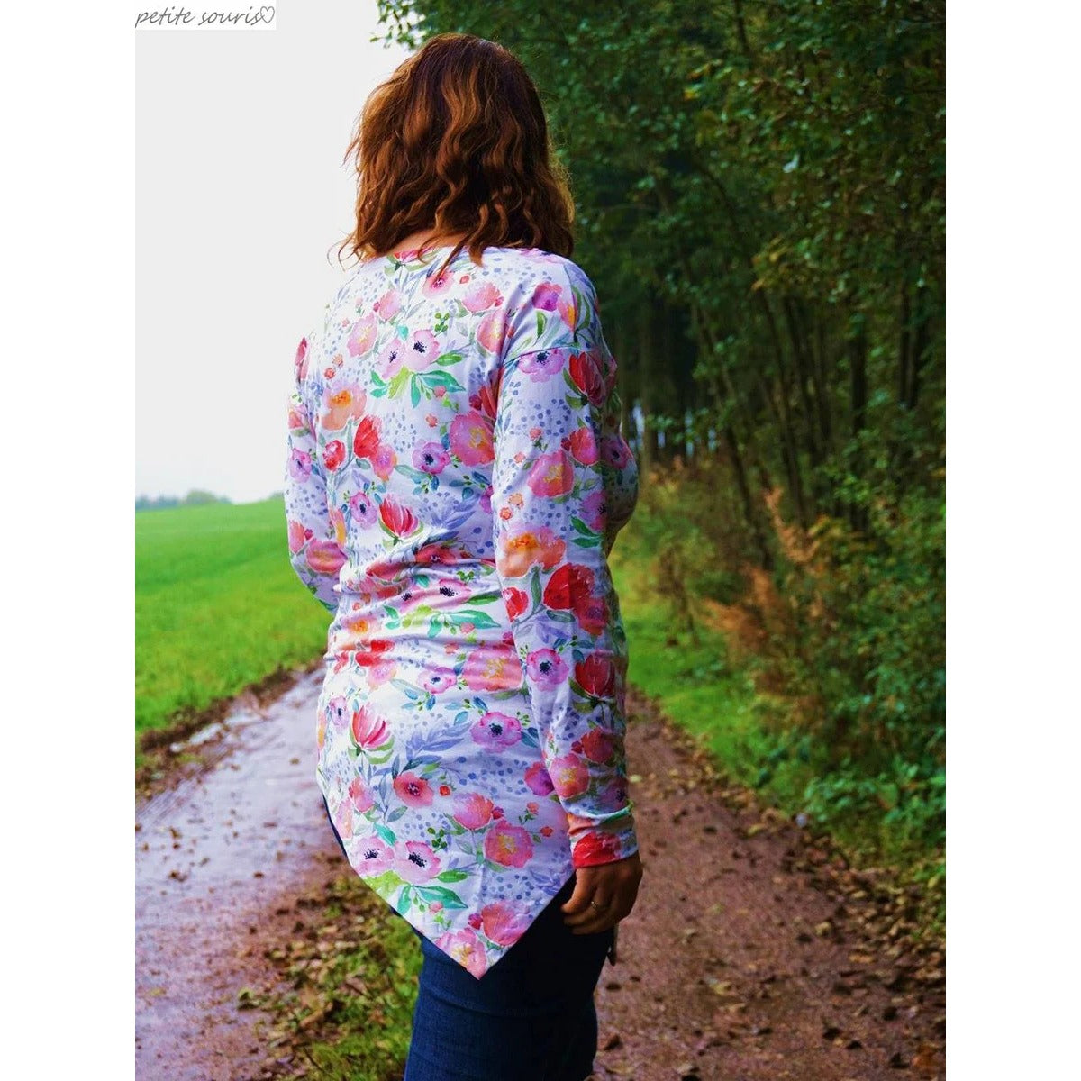 One Tip Shirt Damen als Langarmshirt aus weißem Jersey mit Aquarell-Blumen, Rückansicht mit Zipfelsaum auf einem Waldweg