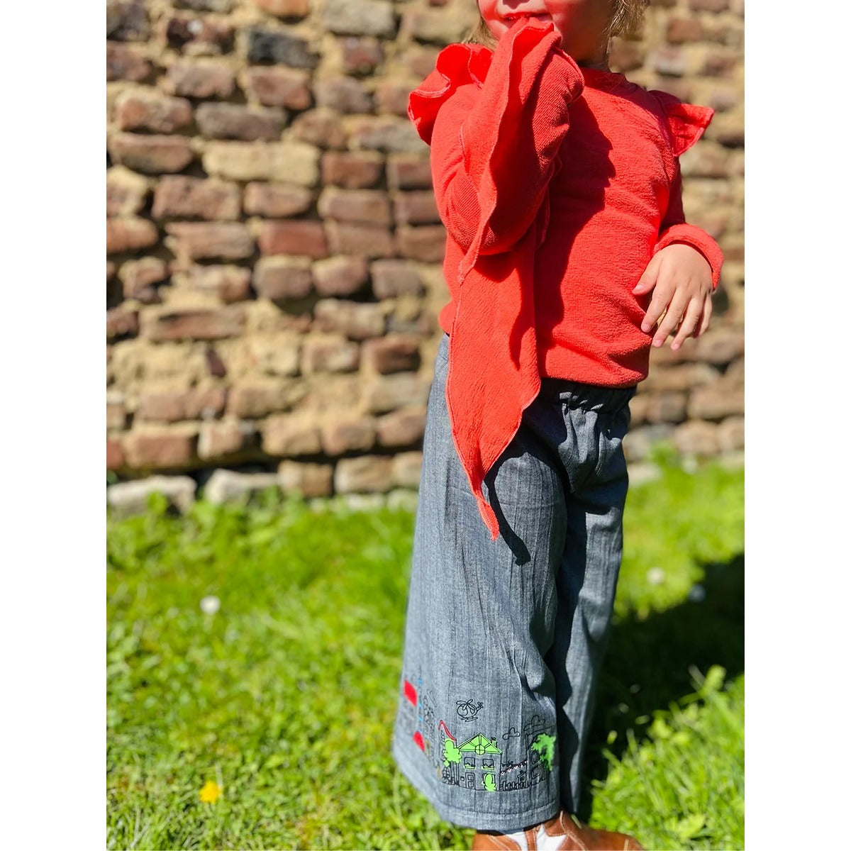 Plisseehose Mädchen – graublaue Plisseehose aus Leinen mit Häuser-Stickerei am Saum, dazu rotes Oberteil mit Volant