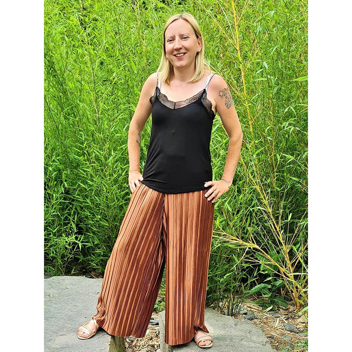 Plisseehose Damen – ockerfarbene Plisseehose mit schwarzem Top, vor Bambus