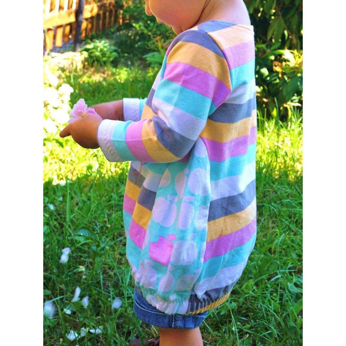 Sidecut Kleid Schnittmuster – pastellfarbene Ballontunika mit Blockstreifen und Apfel-Print, seitliche Ansicht eines Kleinkindes