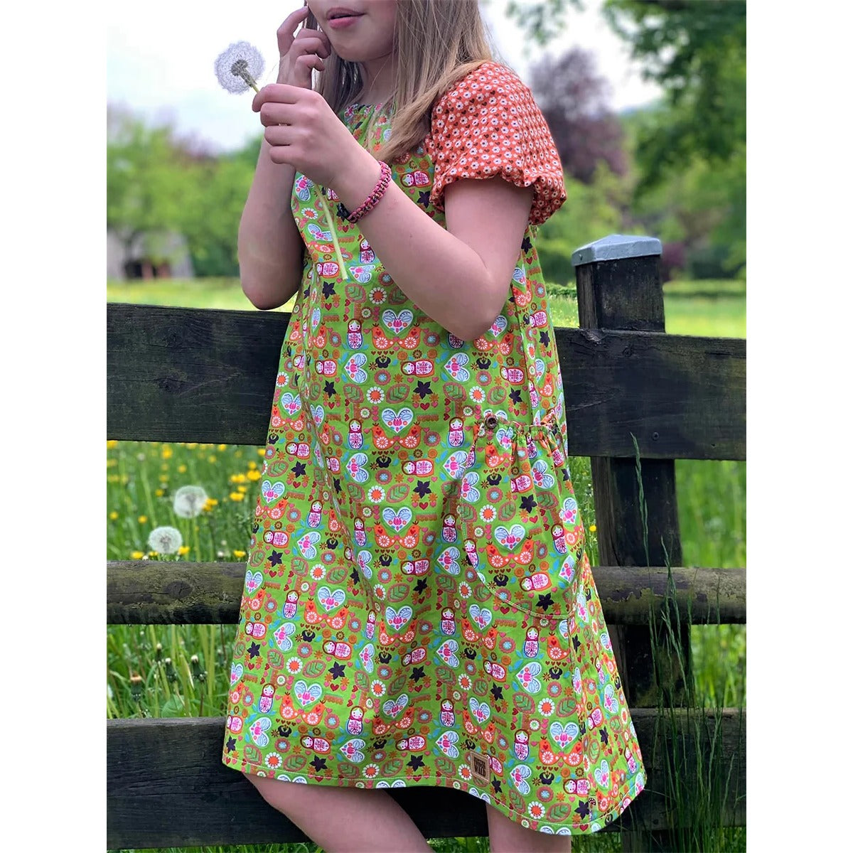 Schnittmuster Talia – grünes Kleid mit Mini-Matroschka-, Blumen- und Herzchen-Print, kurzen Ärmeln mit Gummi und orange geblümten Kontrastärmeln