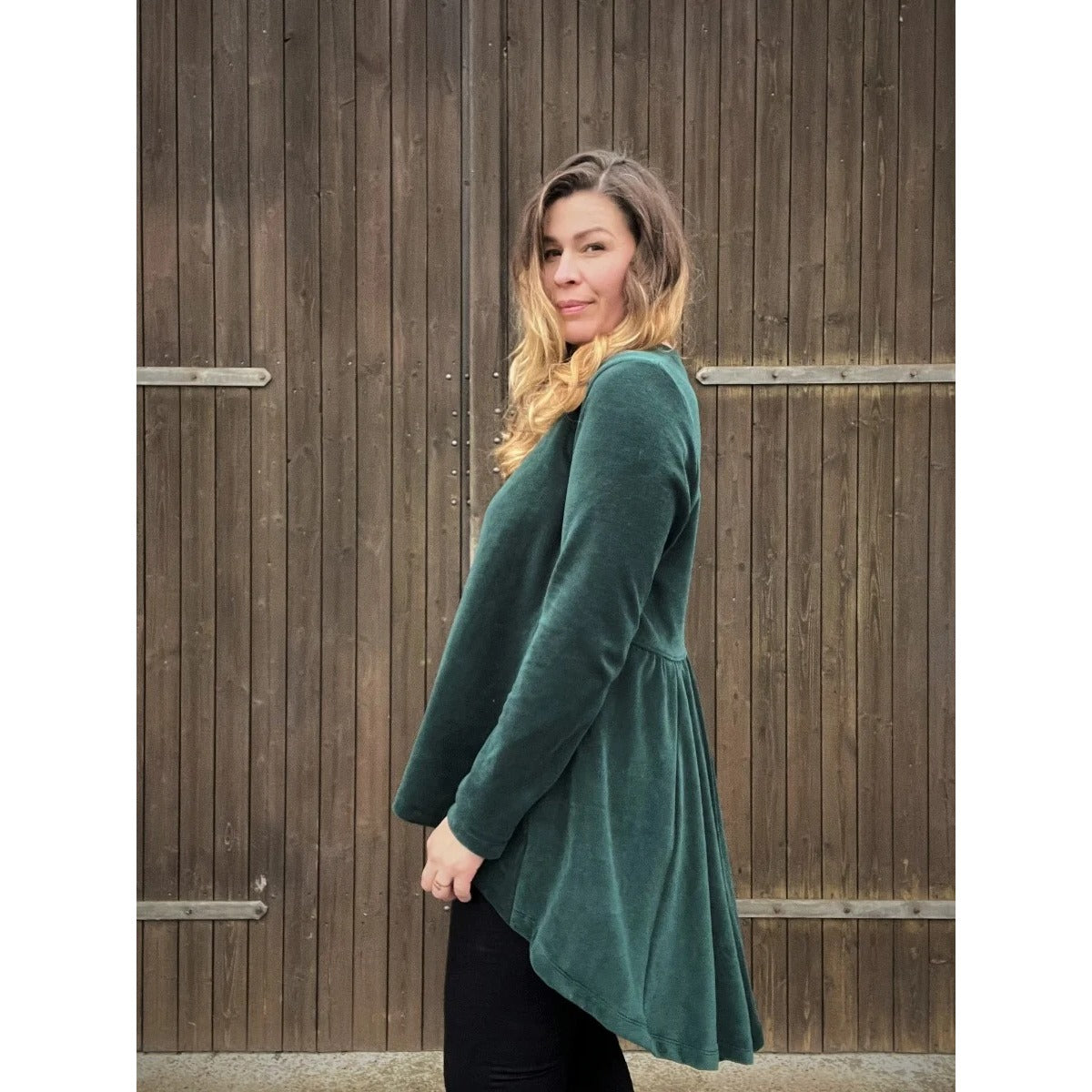 Schößchenshirt Emmelie Schnittmuster – Frau im dunkelgrünen Schößchenshirt vor Holzwand (genähtes Designbeispiel)