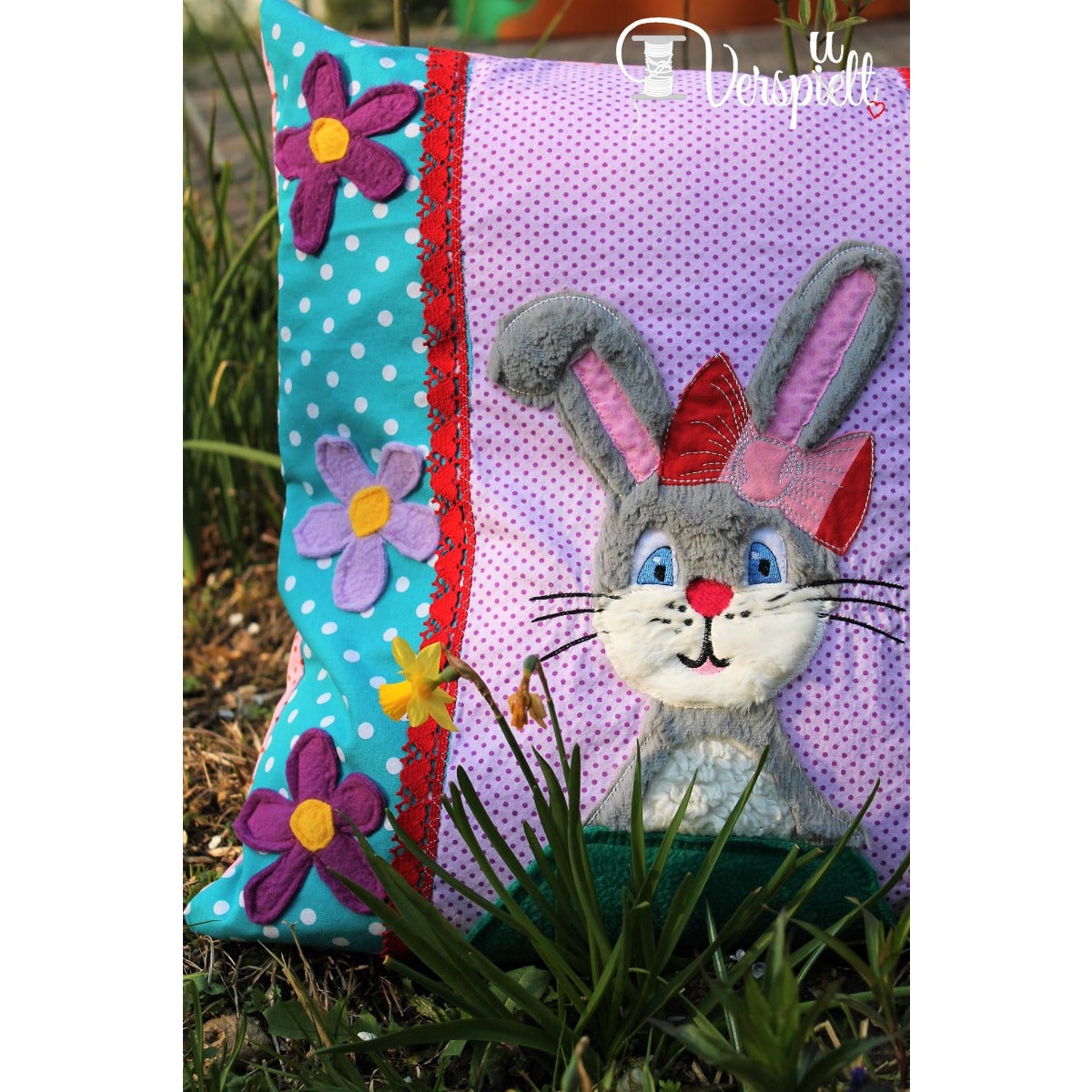 Stickdatei „Emmi Hase“ 13 x 18 cm – Hase als Applikation auf einem lila Kissen mit bunten Bändern