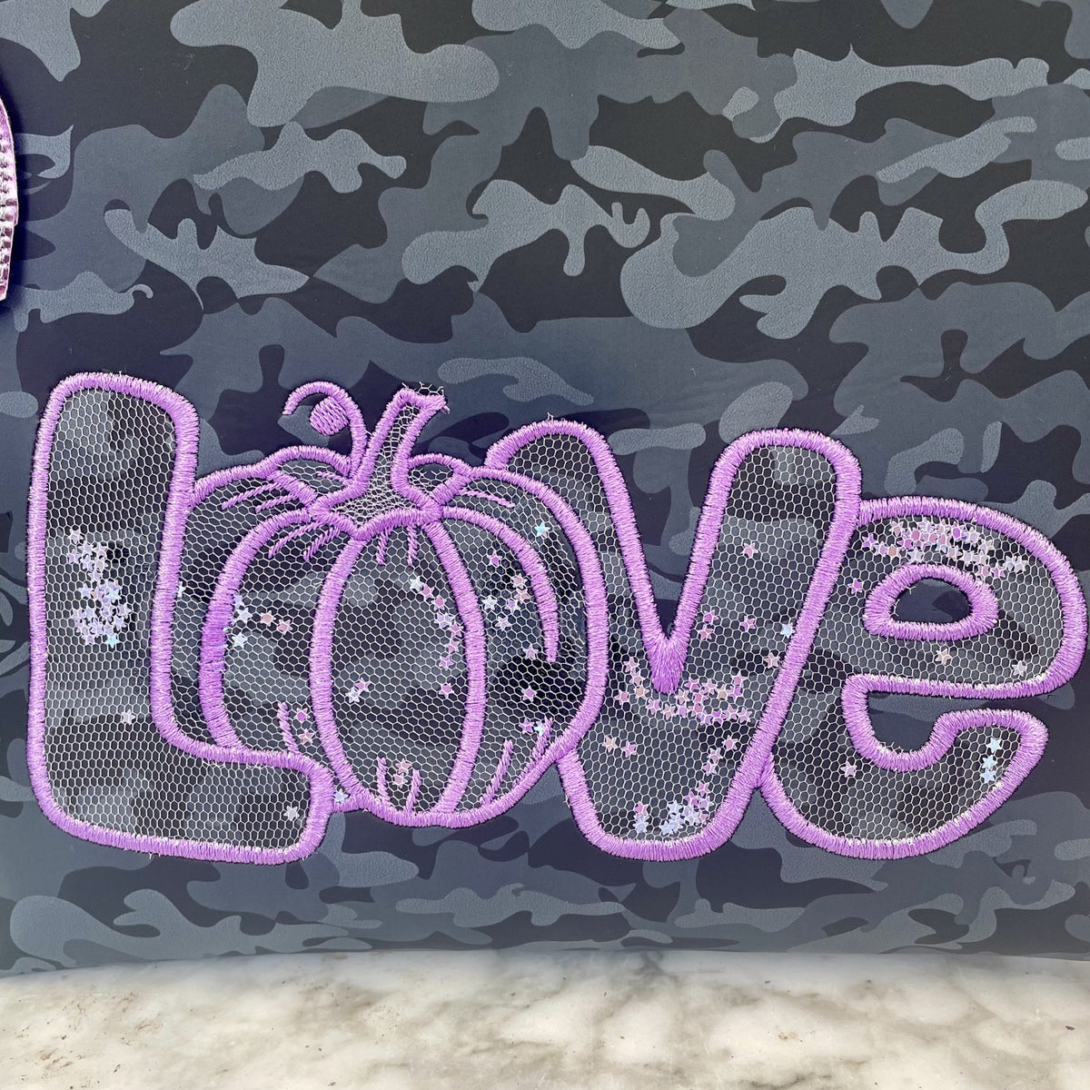 Stickdatei „Kürbis Liebe“ 20 x 30 cm – Nahaufnahme des lila LOVE-Schriftzugs auf Camouflage-Stoff