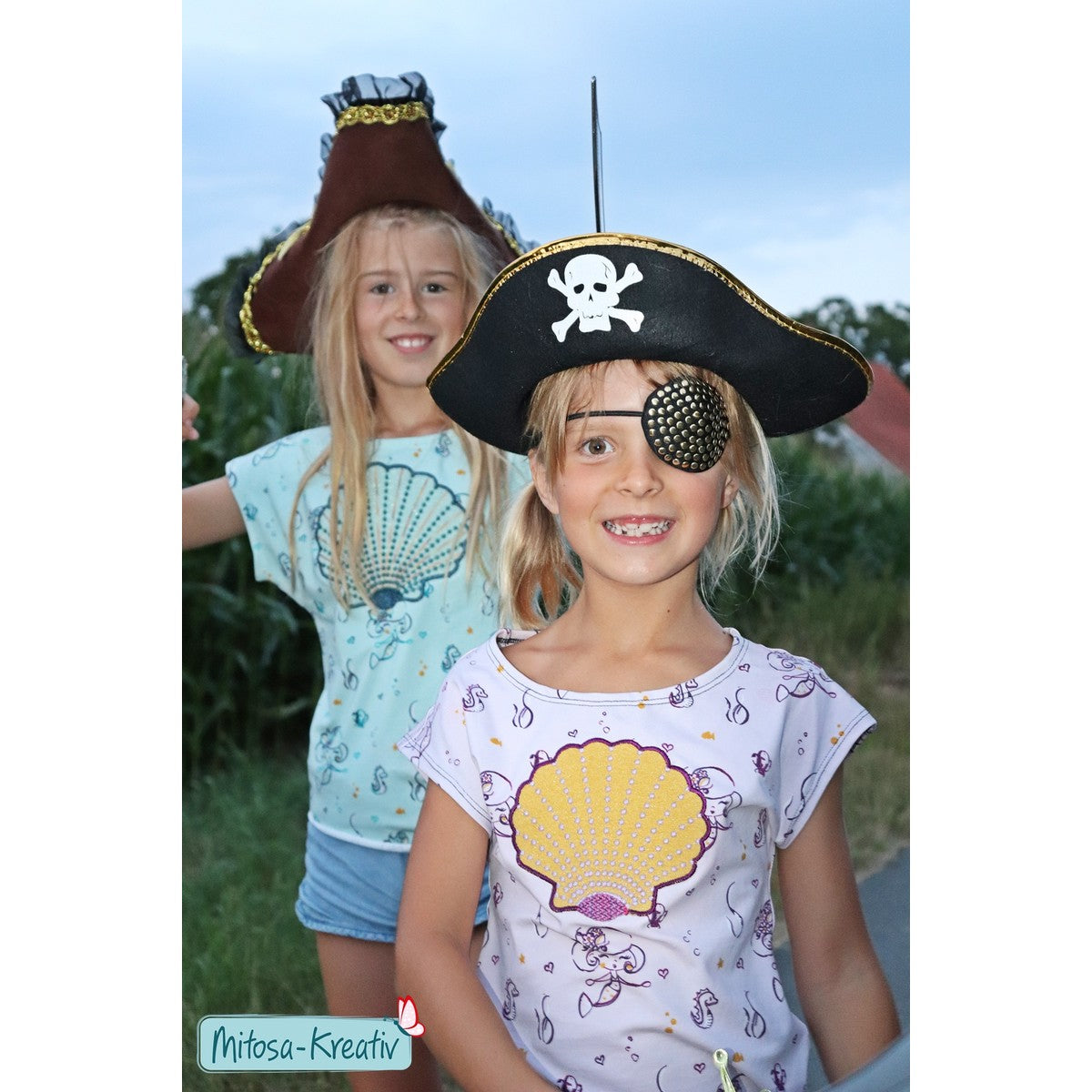 Stickdatei Muschel – Mädchen mit Piratenhut und Augenklappe im Shirt mit gelber Applikations-Muschel, dahinter ein zweites Muschelshirt in Mint