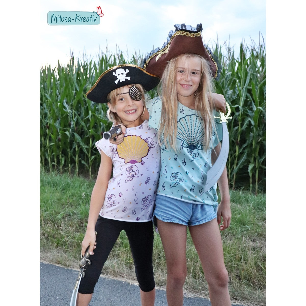 Stickdatei Muschel – zwei Mädchen mit Piratenhüten in Shirts mit Applikations-Muschel in Gelb und in Mint vor einem Maisfeld