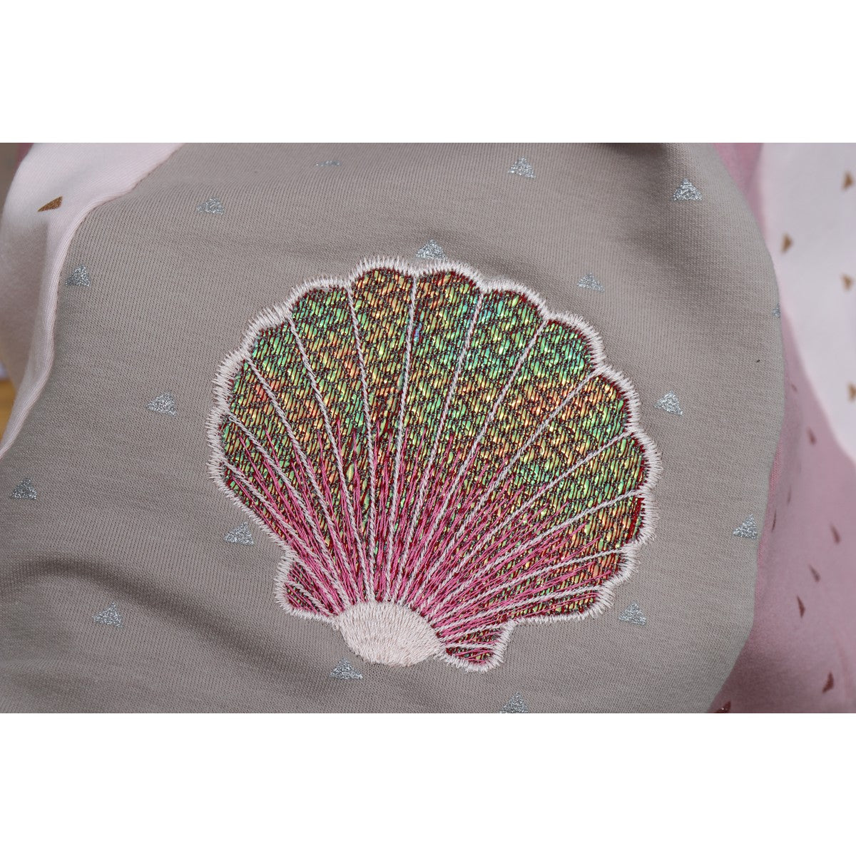 Stickdatei Muschel – bunt schimmernde Folienstick-Muschel auf grauem Stoff, Nahaufnahme