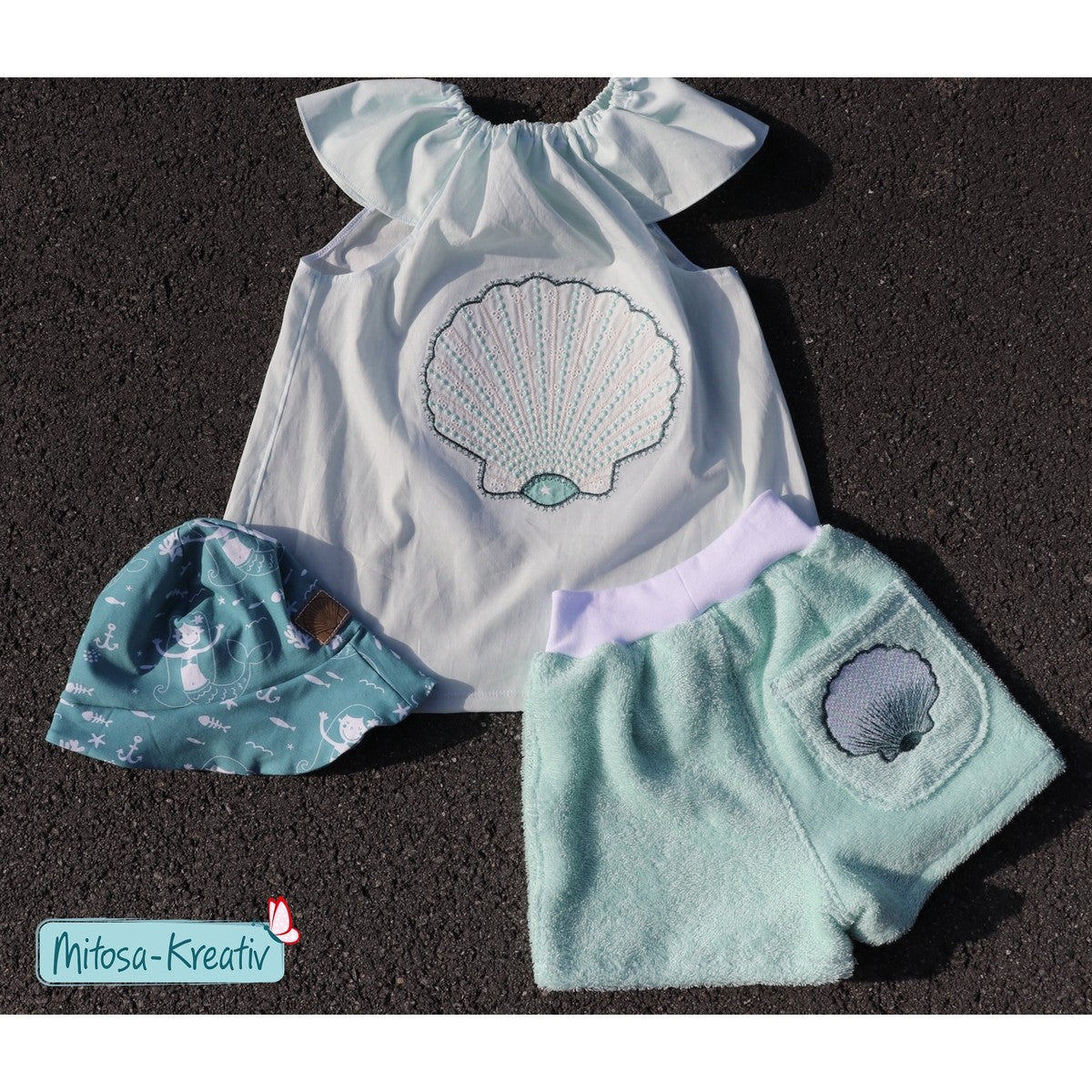 Stickdatei Muschel – weißes Kleid mit großer Sternchen-Applikations-Muschel, daneben Frottee-Shorts mit kleiner Folienstick-Muschel und Sonnenhut
