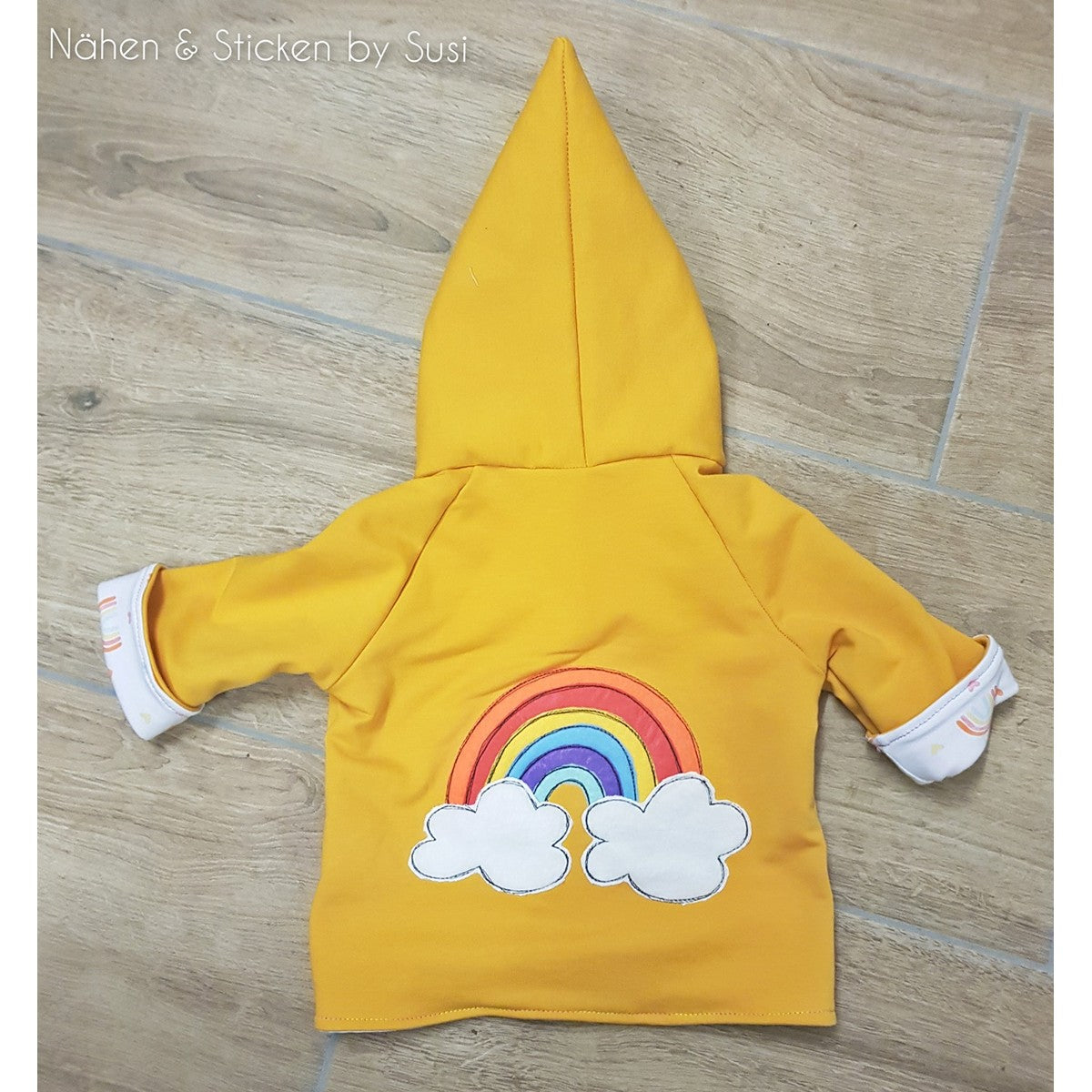 Stickdatei Regenbogen als Applikation auf dem Rücken einer gelben Kinderjacke mit Zipfelkapuze