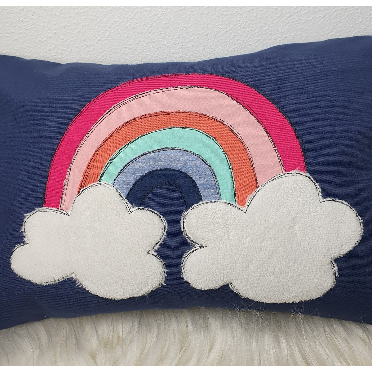 Stickdatei Regenbogen als große Applikation mit weißen Wolken auf einem dunkelblauen Kissen