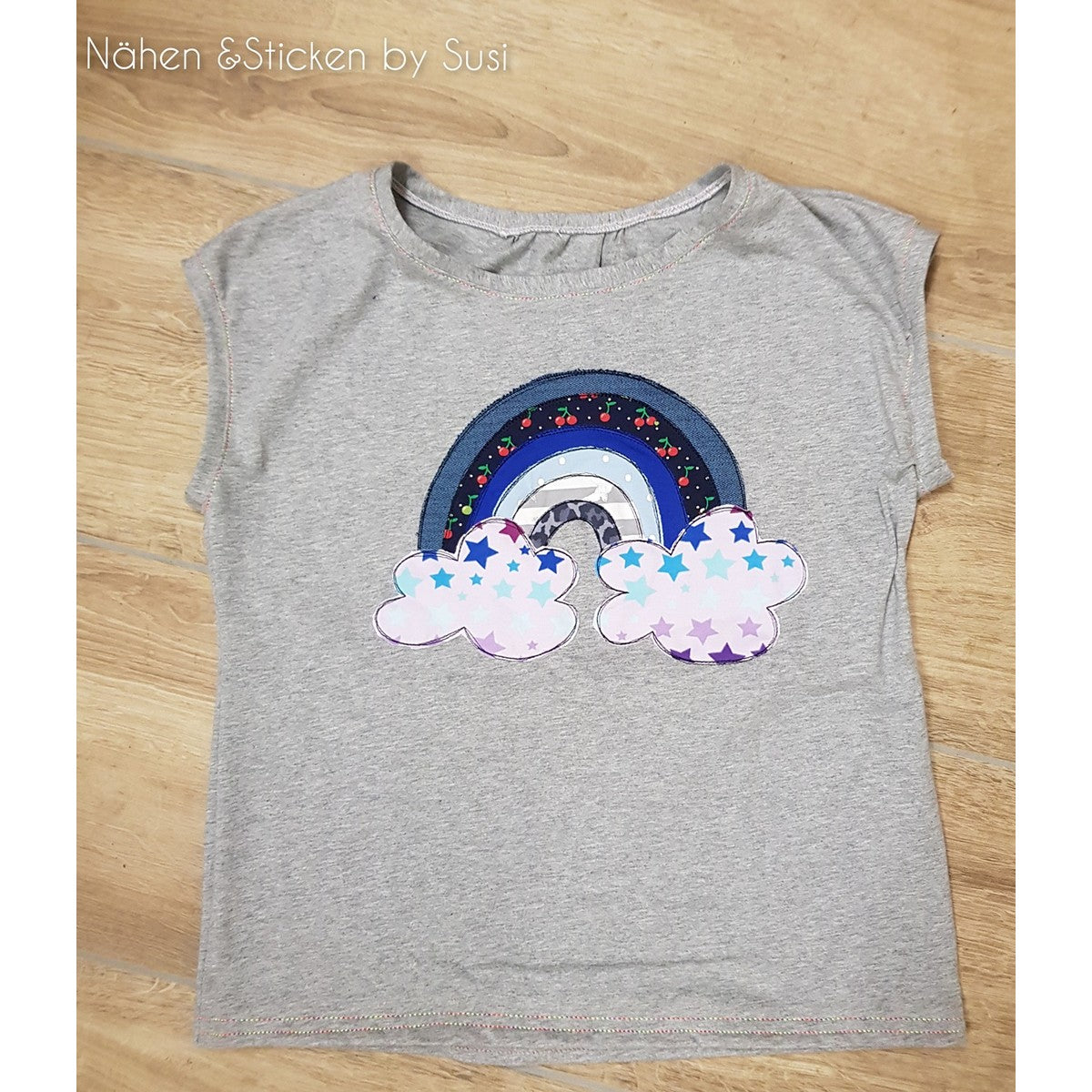 Stickdatei Regenbogen als Applikation in Blautönen mit Sternchenwolken auf einem grauen Shirt