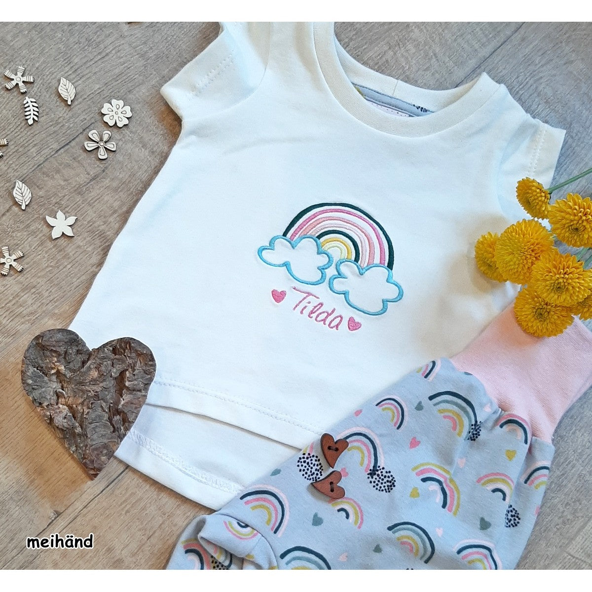 Stickdatei Regenbogen in Pastelltönen auf einem weißen Kindershirt mit gesticktem Namen