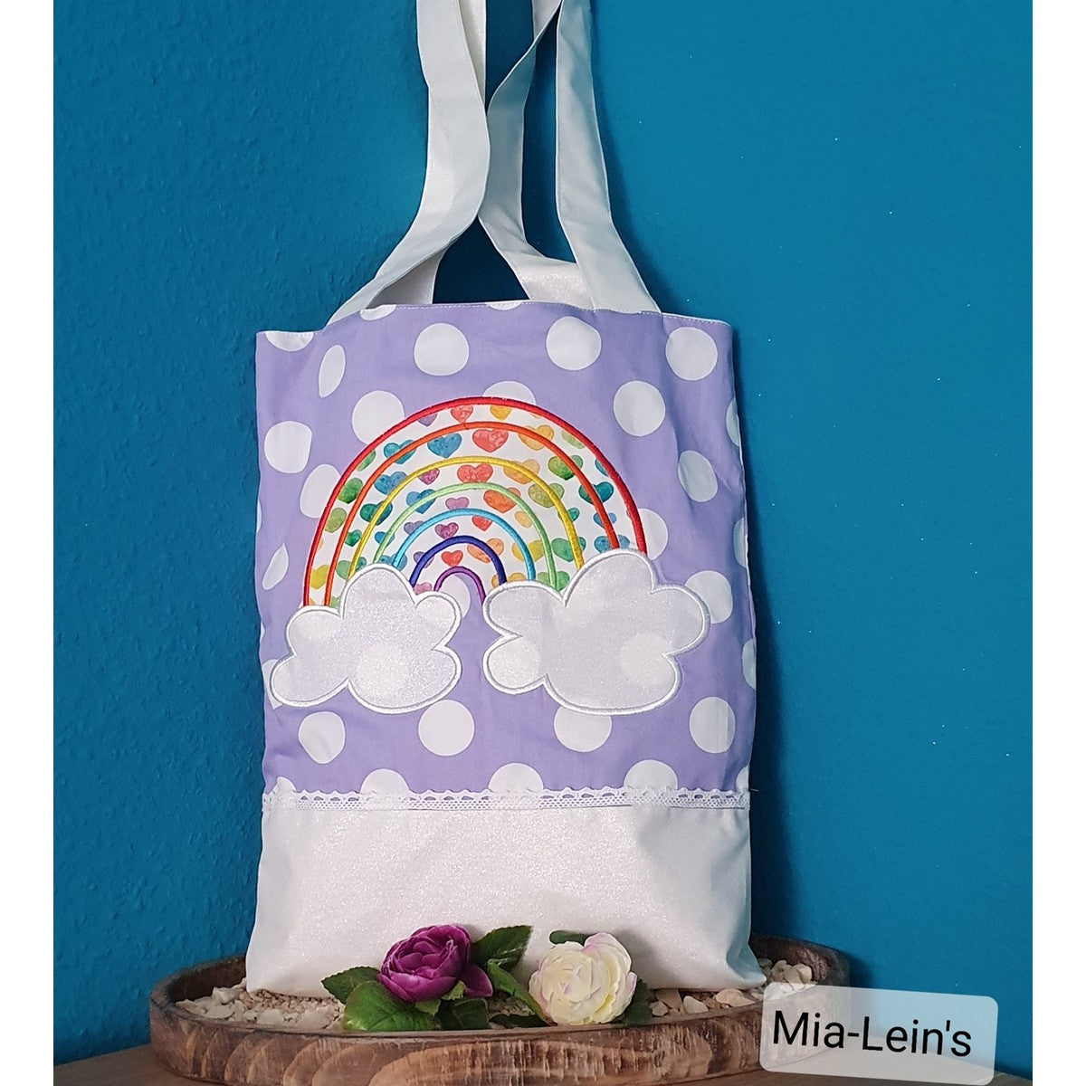 Stickdatei Regenbogen als bunte Applikation auf einem lila gepunkteten Stoffbeutel
