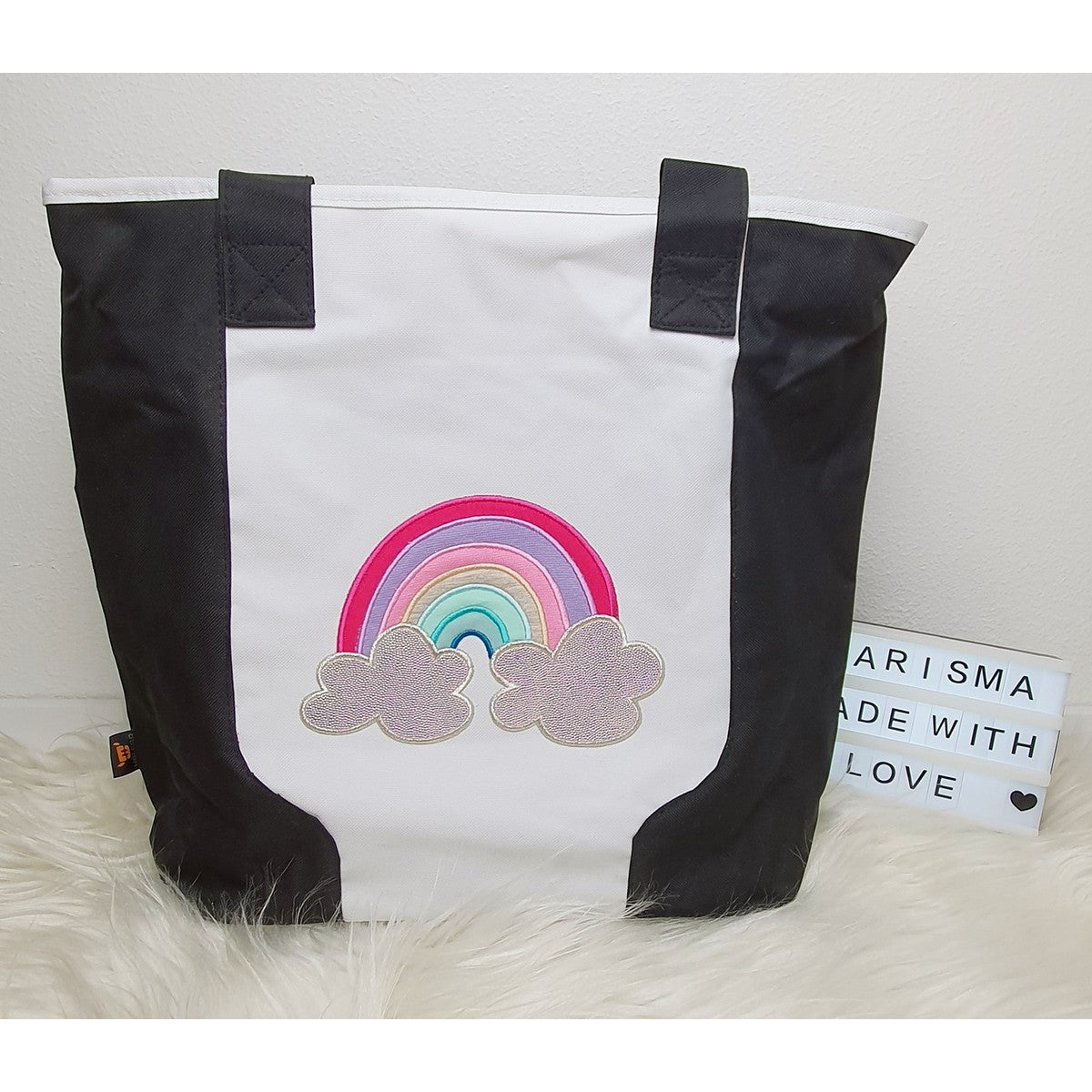 Stickdatei Regenbogen als Applikation in Pink und Pastell auf einer schwarz-weißen Tasche