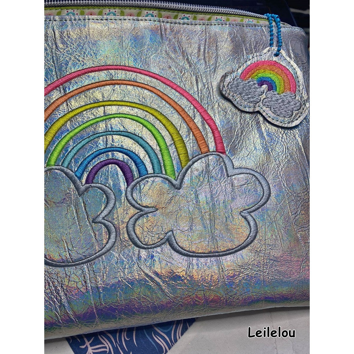 Stickdatei Regenbogen als Sketch-Variante auf einer silbern schimmernden Tasche mit passendem Regenbogen-Anhänger