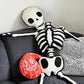 Plotterdatei Lottis Halloween Kürbisse – rotes Kürbiskissen mit weißer Outline neben einem genähten Stoffskelett auf dem Sofa