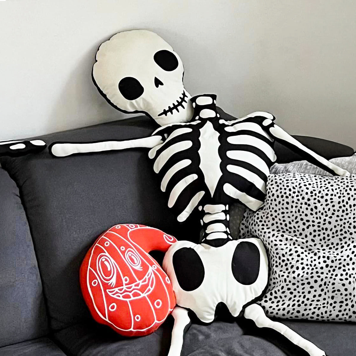 Plotterdatei Lottis Halloween Kürbisse – rotes Kürbiskissen mit weißer Outline neben einem genähten Stoffskelett auf dem Sofa