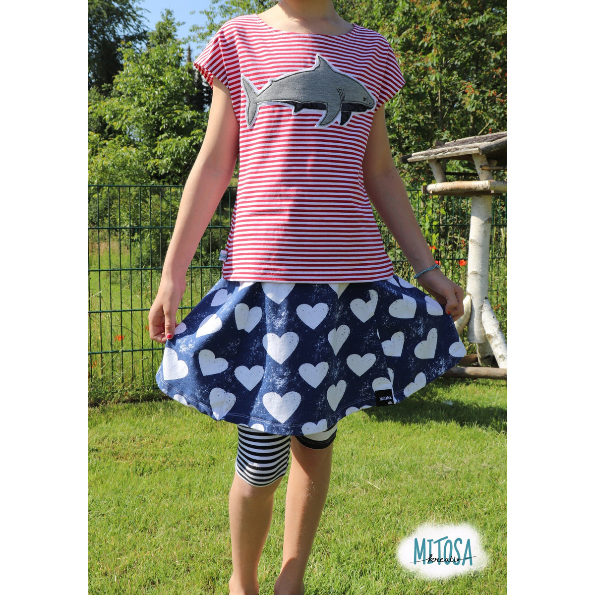 Trapezrock Sandra Schnittmuster – Mädchen im dunkelblauen Herzchen-Rock mit gestreiftem Hai-Shirt (genähtes Designbeispiel)